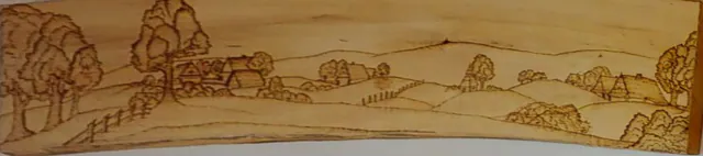 Krajina s kopci, stromy a chalupami vypálená do dlouhého prkna s kůrou