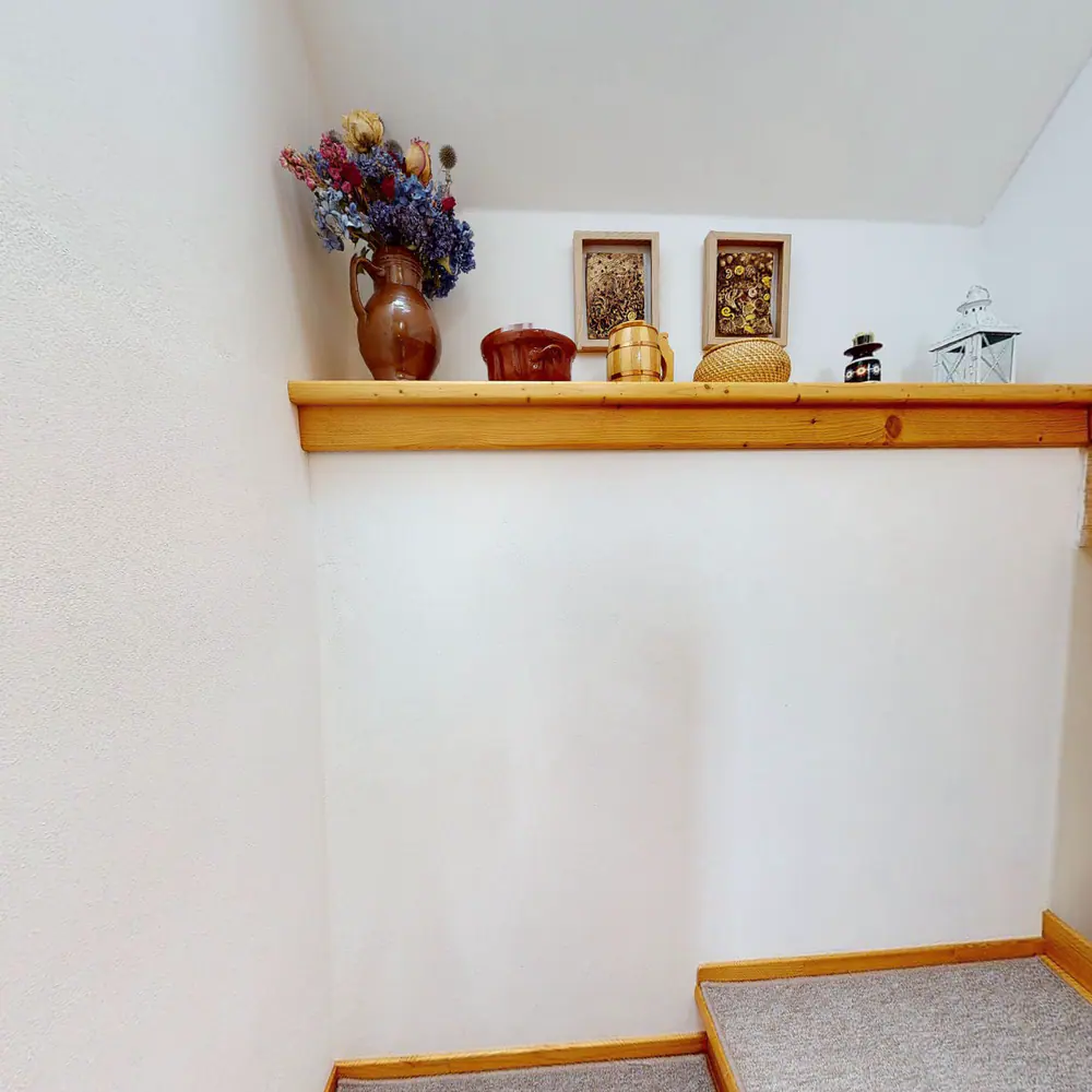 Dřevěné schodiště do podkroví se zábradlím, na podestě police s keramikou.